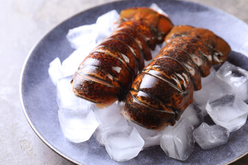 Raw lobster tails with ice on grey table, closeup