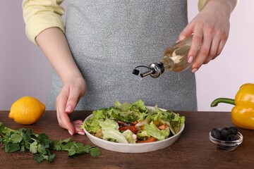 Woman pouring oil onto tasty salad at wooden table against white background, closeup