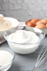 Whipped cream in bowl, sugar, eggs and whisk on gray wooden table, closeup. Cooking meringue cookies
