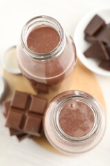Tasty chocolate milk and pieces on white table, flat lay