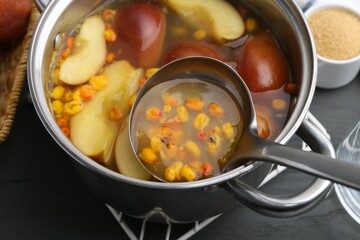 Taking tasty compot with ladle from pot on grey wooden table, closeup