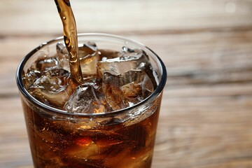 Pouring refreshing cola into glass on blurred background, closeup. Space for text