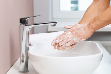 Woman washing her hands with foaming soap above sink in bathroom, closeup