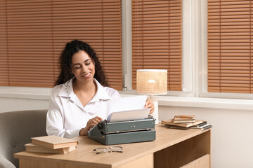 Young African-American woman using typewriter and sitting at table at home