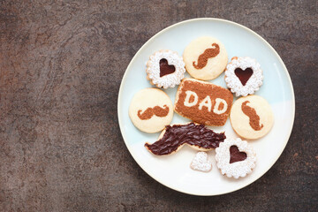Plate of Fathers Day cookies. Overhead view on a dark stone background. Chocolate mustache, heart and dad cookies.