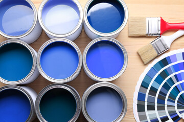 Cans with paint in shades of blue, color palette and brushes on wooden background, top view