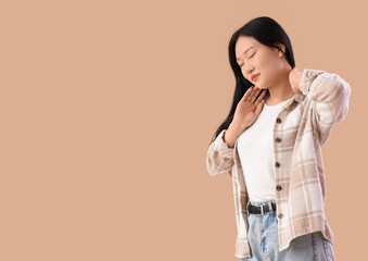 Beautiful young Asian woman suffering from back pain on beige background