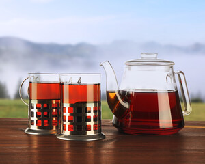 Glasses of freshly brewed tea in holders and teapot on table in mountains outdoors