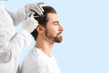 Handsome man receiving injection for hair growth on blue background, closeup