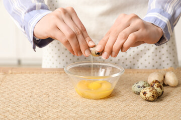 Woman breaking quail eggs into glass bowl at table, closeup