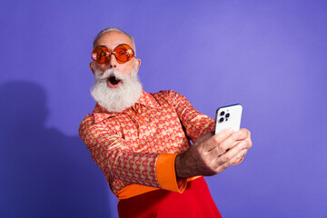 Happy elder with grey beard taking selfie in retro fashion on purple background, showcasing fun charisma
