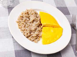 Boiled pearl barley with omelette served on dish on a checkered cloth