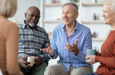 Multiethnic elderly people attending group therapy session at nursing house, positive senior man and woman sitting in circle, drinking tea and having conversation with psychologist, closeup