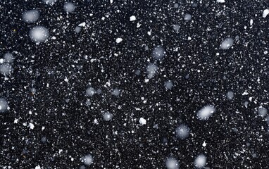 Light snowfall on dark surface. Tiny white flakes scattered across a dark gray backdrop, creating a wintery scene