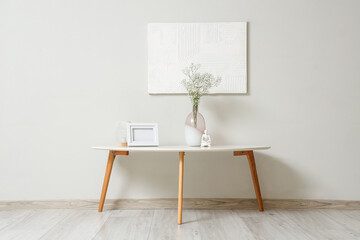 Coffee table with decor and gypsophila flowers in vase near grey wall in room