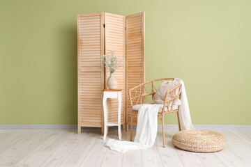 Gypsophila flowers in vase, armchair and folding screen near green wall in room