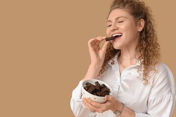 Beautiful young woman with box of sweet chocolate candies on beige background