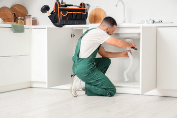 Male plumber repairing sink pipe in kitchen