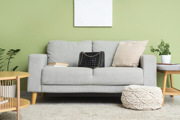 Stylish bag with books on grey sofa in living room