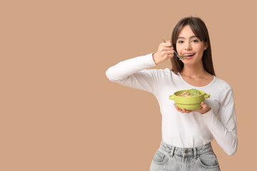 Young woman eating tasty granola with kiwi on beige background