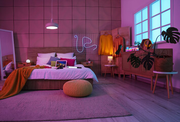 Comfortable bed with laptop and glowing lamps late in evening