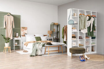 Interior of light bedroom with shelving unit and clothes