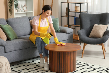 Young woman wiping table with rag and spray in living room