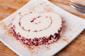On dessert plate is slice of roll made from soft cream cheese and cranberries. Sweet curd dessert, delicate delicacy