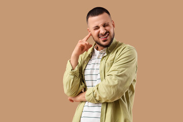 Young man suffering from loud noise on beige background