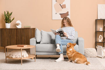 Young woman reading magazine with Corgi dog in living room
