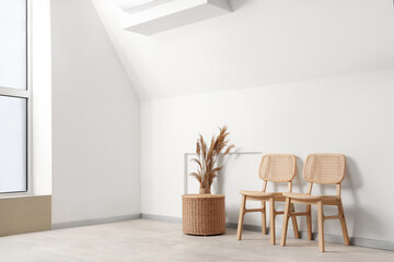 Chairs, basket and pampas grass in vase near white wall in room