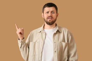 Shocked young man pointing at something on beige background