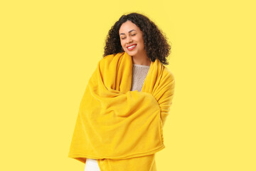 Fototapeta premium Beautiful young African-American woman with cozy blanket on yellow background