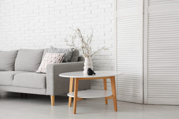 Interior of stylish living room with grey sofa, folding screen and blooming tree branches on coffee...