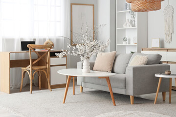 Interior of light living room with sofa, table and blossoming branches in vase