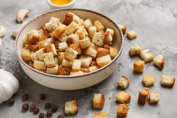 Bowl with crunchy croutons, peppercorns and garlic on grey background, closeup