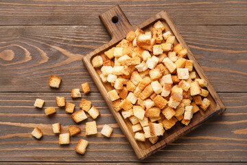Cutting board with crunchy croutons on wooden background