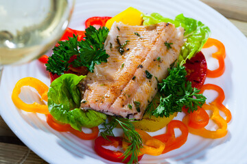 Delicious roasted juicy trout fillet served with fresh vegetables and greens