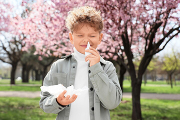 Sick little boy with nasal drops and tissue suffering from allergy outdoors