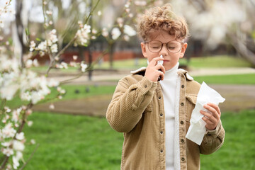 Sick little boy with tissue and nasal drops suffering from allergy outdoors