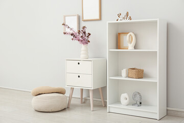 Fototapeta premium Dresser with shelving unit, different decor and vase of pink blooming branches near white wall in living room