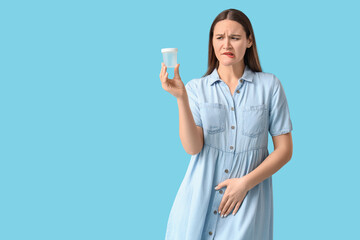 Young woman with urine collection container on blue background. Cystitis concept