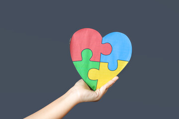 Child Hand Holding Colorful Heart on Gray Background. World Autism Awareness Day Concept.
