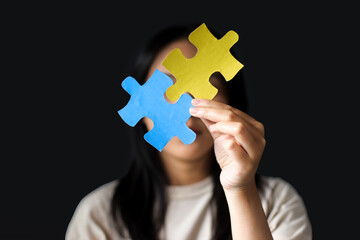 Teenager Girl Cover Her Face With Colorful Puzzles Pieces on Dark Background