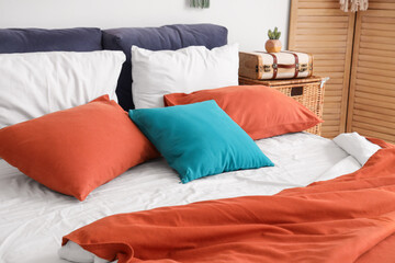 Cozy bed with soft colorful pillows and red blanket in bedroom
