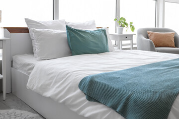 Interior of light bedroom with cozy bed and grey armchair near big window