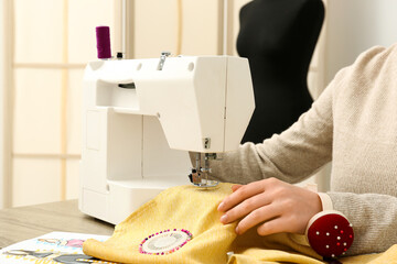 Female tailor sewing yellow clothes at table in atelier, closeup