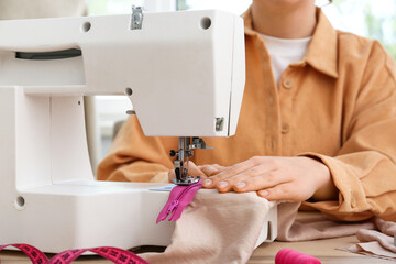 Female tailor sewing zipper at table in atelier, closeup