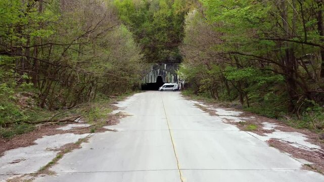 Aerial pullback down remote road from hidden Zeljava airbase entrance carved into a mountain as tour vehicle reverses