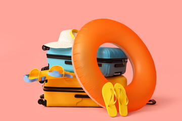 Suitcases, inflatable ring, flippers, straw hat and flip-flops on pink background